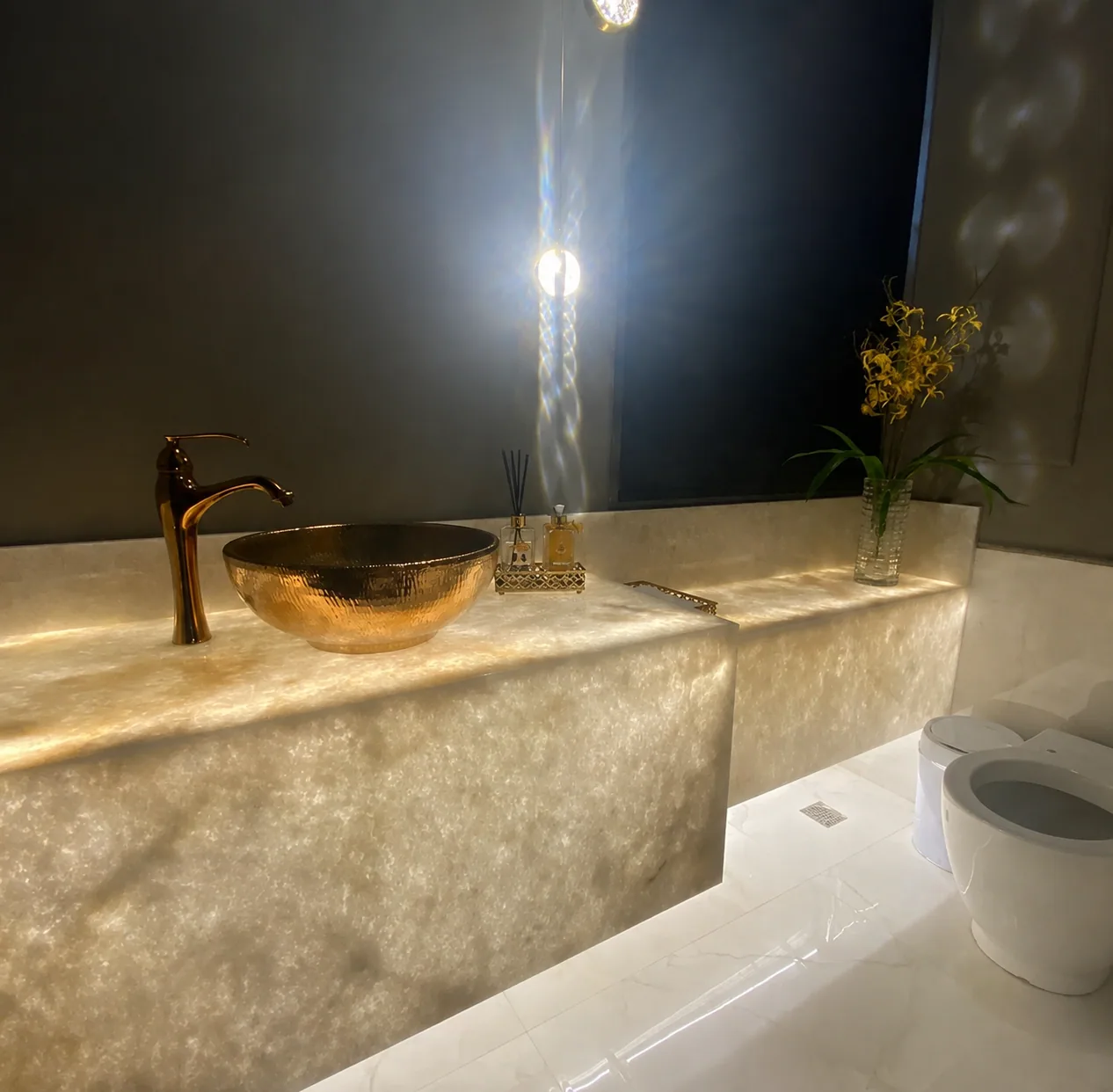 Lavabo com bancada de onix retroiluminado e cuba dourada, executado pela Baltazar Marmores e Granitos